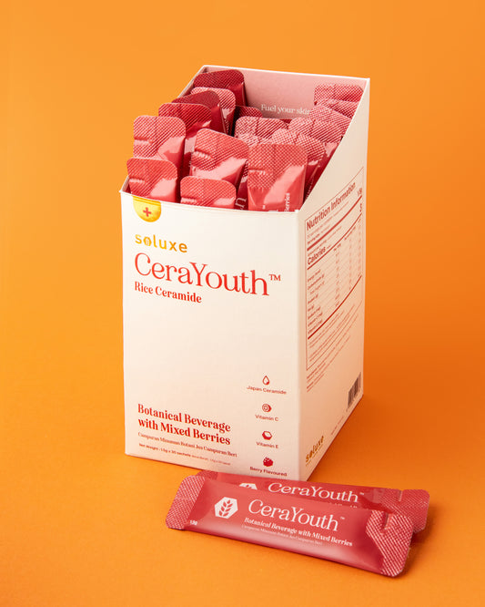 A box of Soluxe CeraYouth beauty powder with individual sachets visible, predominantly in a pink hue against an orange background.