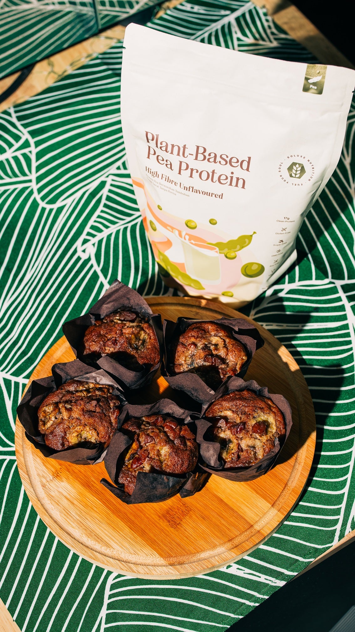 Muffins on a wooden board with a bag of unflavoured plant-based pea protein in the background.