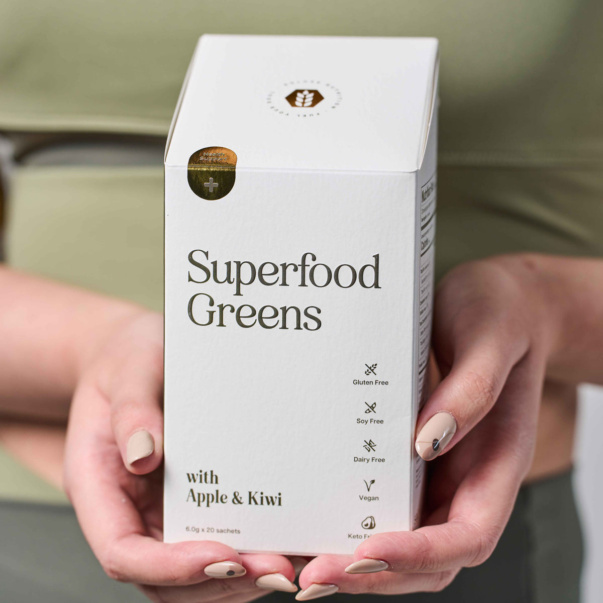 Box of 'Superfood Greens with Apple & Kiwi' held by hands against a neutral background