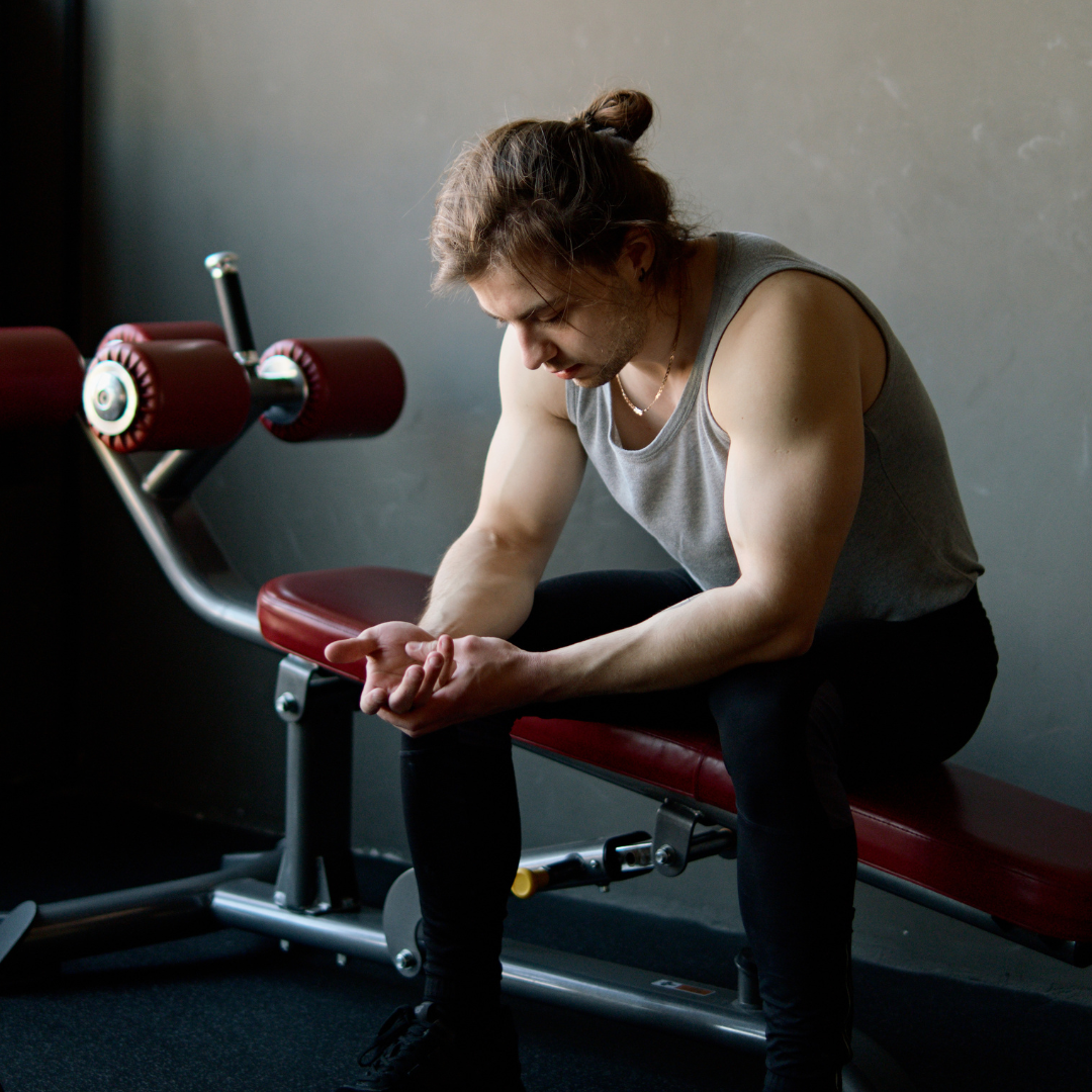Man sitting on a weight bench in a gym, preparing for exercise.