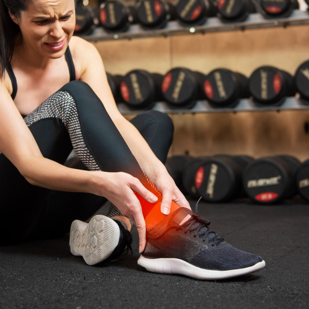 Woman experiencing pain in a gym setting, holding her foot.