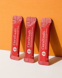 A box of Soluxe CeraYouth beauty powder with individual sachets visible, predominantly in a pink hue against an orange background.